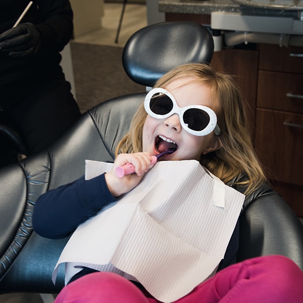 A little girl lying in the dentist's chair at Neighborhood Dental while learning to brush her teeth